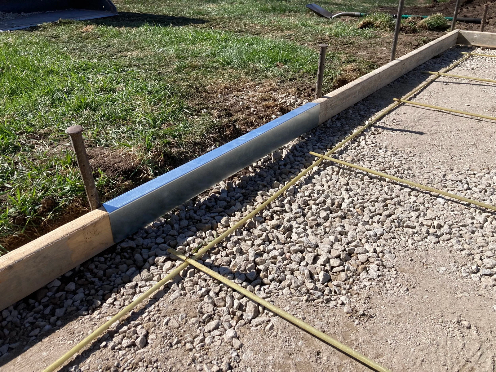 Concrete foundation with wooden forms and gravel, surrounded by grass.