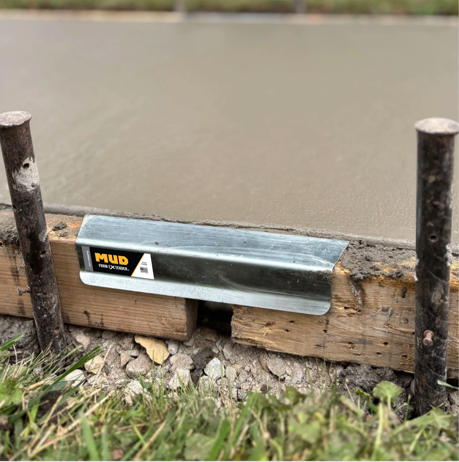Metal strip with 'MUD' branding embedded in concrete, surrounded by grass and dirt.