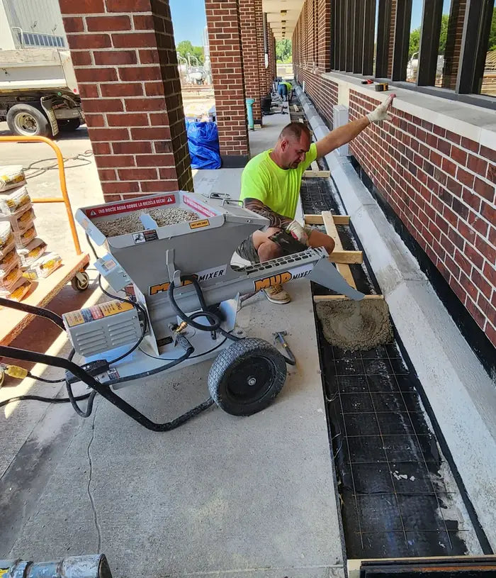 Contractor pouring a footing along a brick wall with a MudMixer
